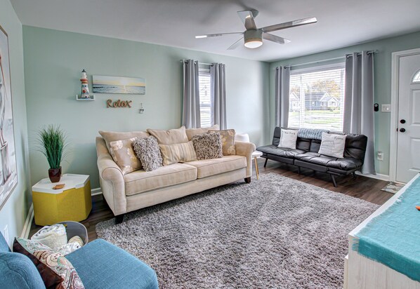 A living room with a beige sofa, a black leather sofa, a large rug, and a ceiling fan.