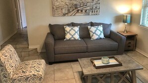 Un salon avec un canapé gris, un fauteuil à motifs et une table basse agrémentée d’objets décoratifs.