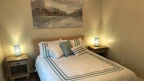 Une chambre à coucher comprenant un lit, deux tables de chevet, une commode et un tableau accroché au mur.