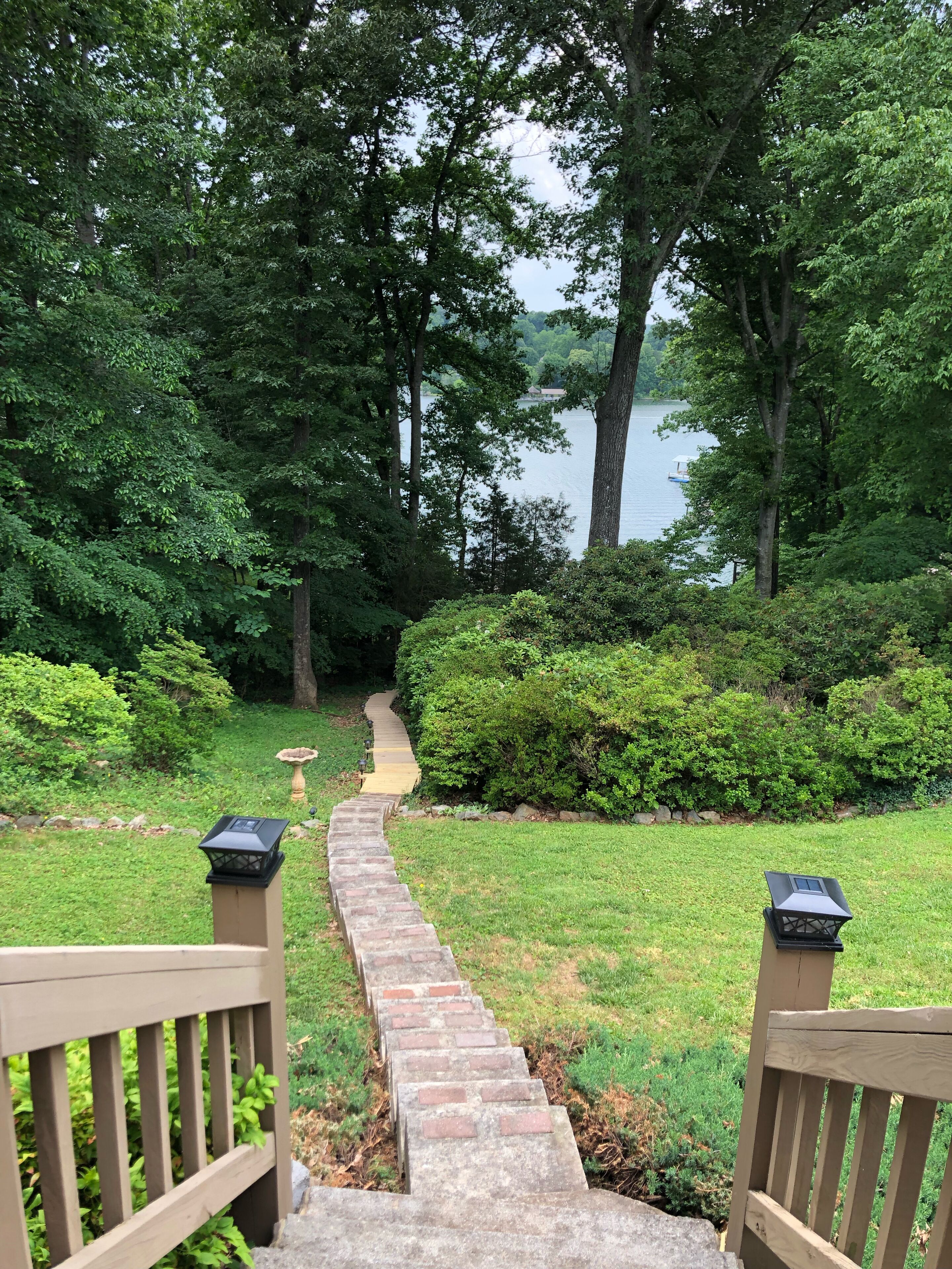 A stone pathway leading to a lake, surrounded by lush greenery and trees.