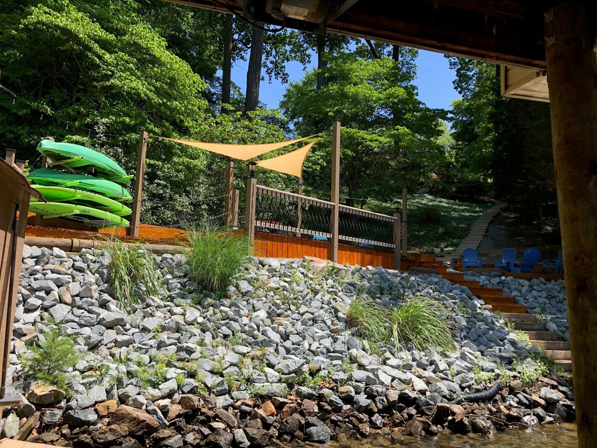 Un espace extérieur rocheux, délimité par une clôture en bois, une barrière en corde et où l’on peut voir des kayaks verts.
