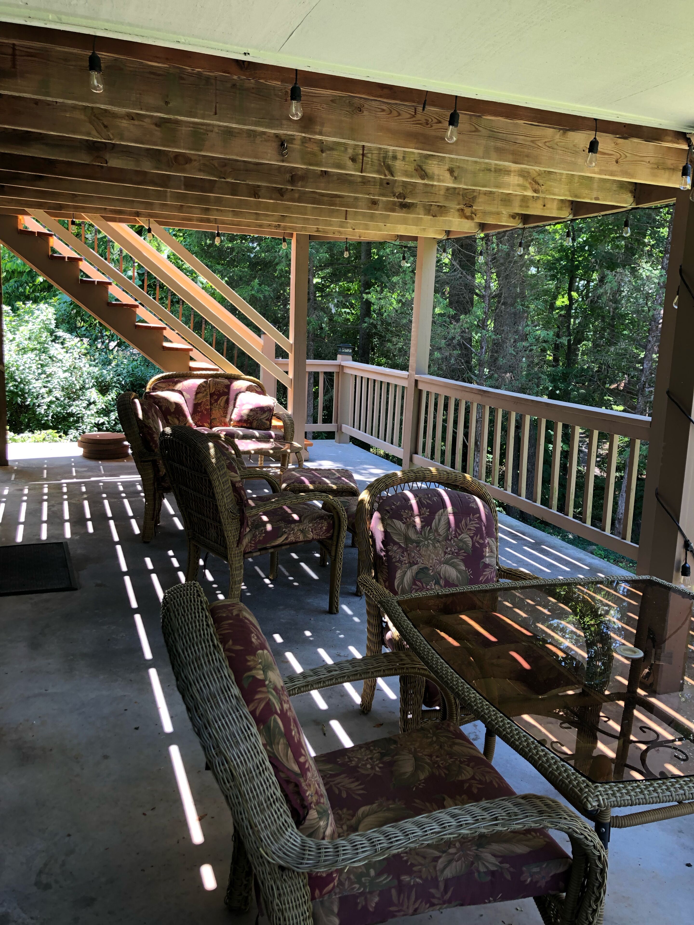 Un espace extérieur aménagé, abrité et doté de meubles en osier, avec un escalier en bois menant à une terrasse.