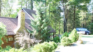 Ein rustikales Blockhaus mit Steinkamin, umgeben von dichtem Wald und einem Kiesweg.