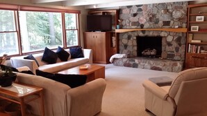 Una sala de estar acogedora con chimenea de piedra, un televisor sobre un mueble de madera, un sofá con cojines y una estantería.