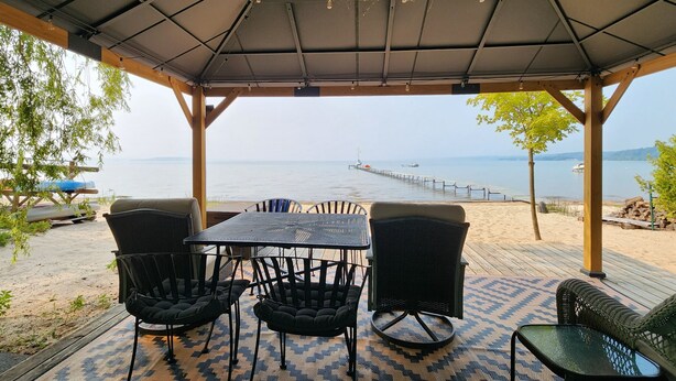 Un espacio de estar techado al aire libre con una mesa y sillas, con vista a una playa y al mar.