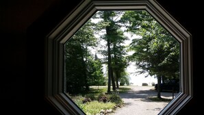 Vista a través de una ventana con marco geométrico, que muestra un sendero bordeado de árboles y una zona de grava.