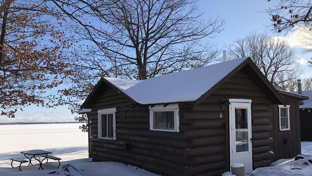 Une cabane en rondins dont le toit est recouvert de neige, avec une porte et des fenêtres.