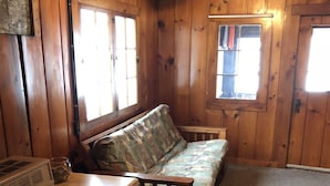 L’intérieur d’un chalet accueillant, avec un plancher en bois, un canapé, un fauteuil et une petite table.