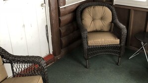 L’intérieur d’une cabane en rondins, avec des meubles en osier, une moquette verte et une fenêtre équipée de stores.