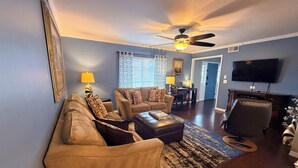 A living room with a sofa set, a coffee table, a rug, a TV, and a ceiling fan. - Hot Tub, Pool, Game Room & Mini Golf + 2 King Beds, Fun For the Whole Family! (Tampa)