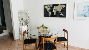 Ein Essbereich mit einem runden Glastisch, umgeben von Holzstühlen mit schwarzen Kissen. Über dem Tisch ist eine Weltkarte an der Wand angebracht.