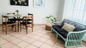 Ein Essbereich mit einem runden Glastisch und Holzstühlen, einer grün gepolsterten Couch, einem gewebten Korb sowie einer Weltkarte und einem Gemälde von Pferden an der Wand.