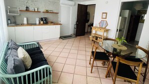 Ein kompakter Wohnbereich mit Küchenzeile, einem Essbereich mit Glastisch und einer Sitzecke mit Sofa und Sesseln.