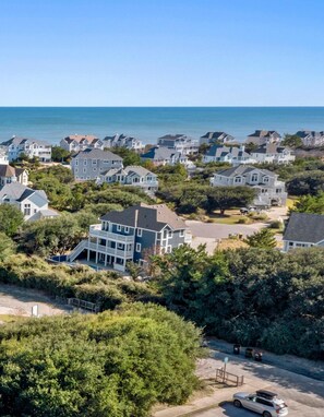 A coastal residential area with houses, a clear view of the ocean, and a parking area with a car.