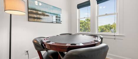 Un salón de conferencias con una mesa redonda, cuatro sillas, una lámpara de pie, un cuadro y ventanas con cortinas azules.