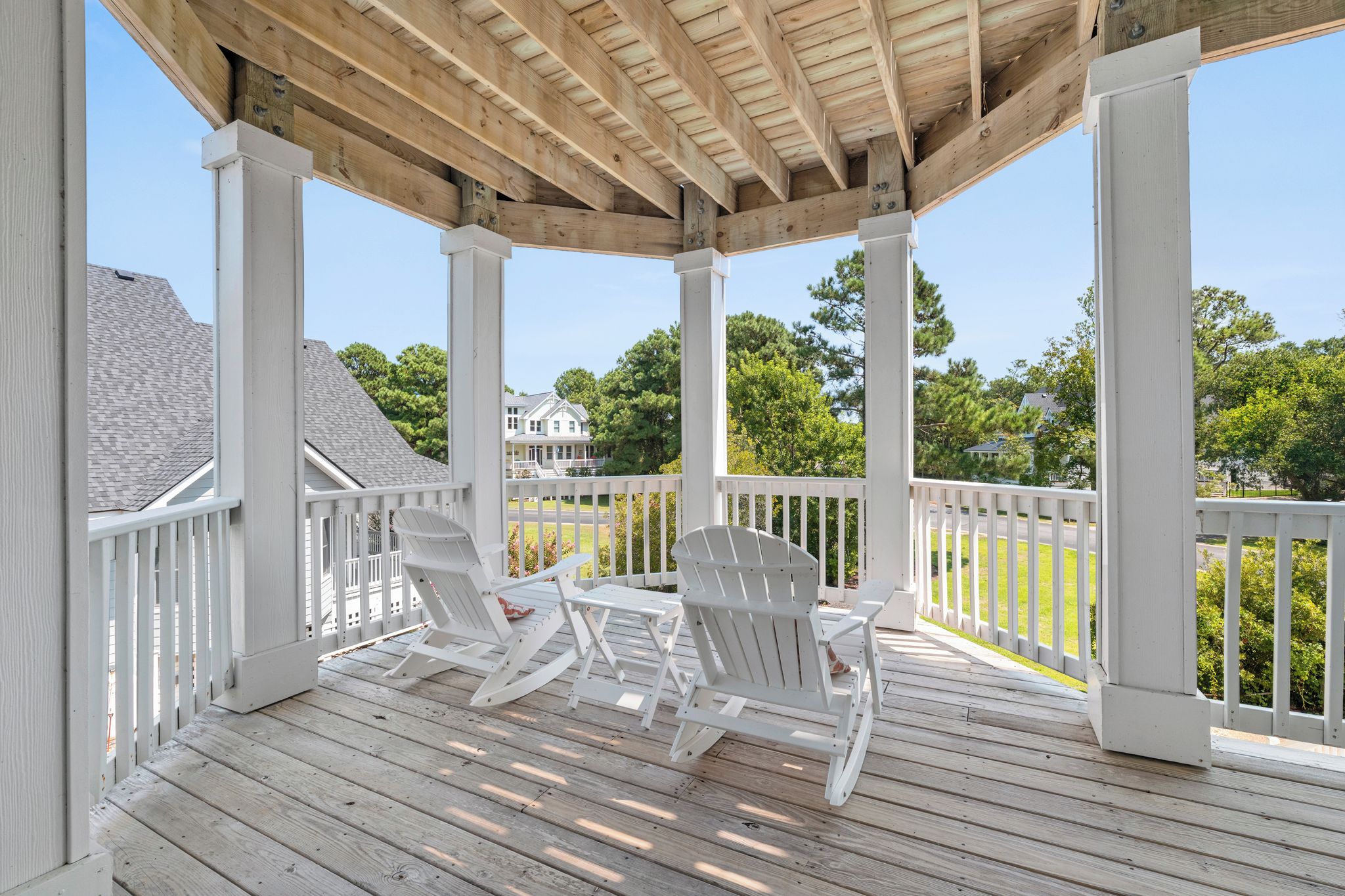 A covered outdoor area with wooden flooring, white railings, and Adirondack chairs.