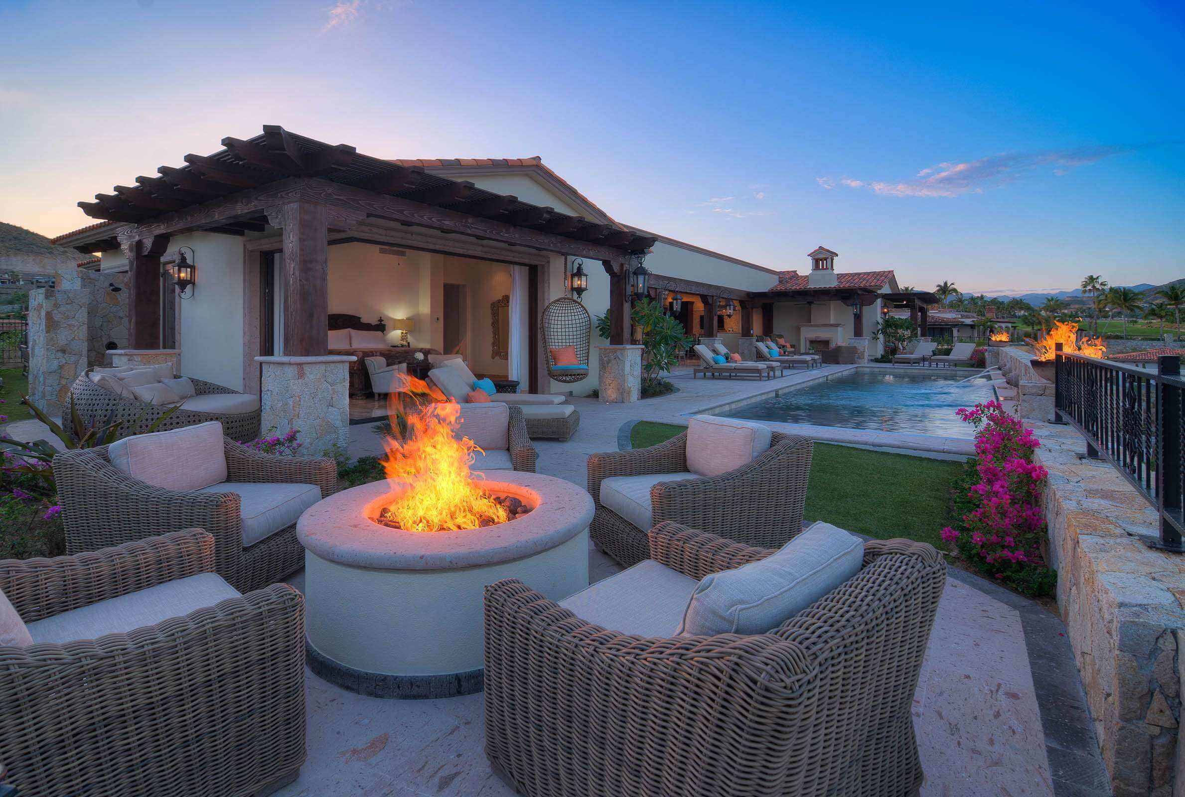 A poolside area with wicker furniture, a fire pit, and a view of a pool and mountains.