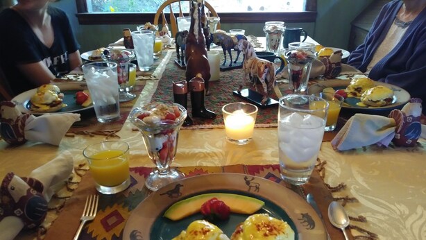 A dining table with breakfast items, including eggs benedict, fruit, and beverages.