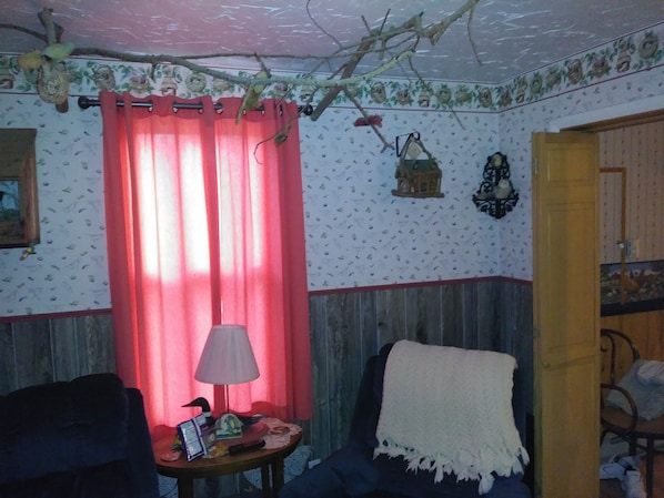 A room with a wooden floor, a red curtain, a lamp on a side table, and a chair with a white throw blanket. - Anchorage Farm B&B (Pine)