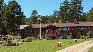 A lodge with a red-tiled roof, a flagpole with an American flag, a wooden staircase, and a well-maintained garden with potted plants and a bench.