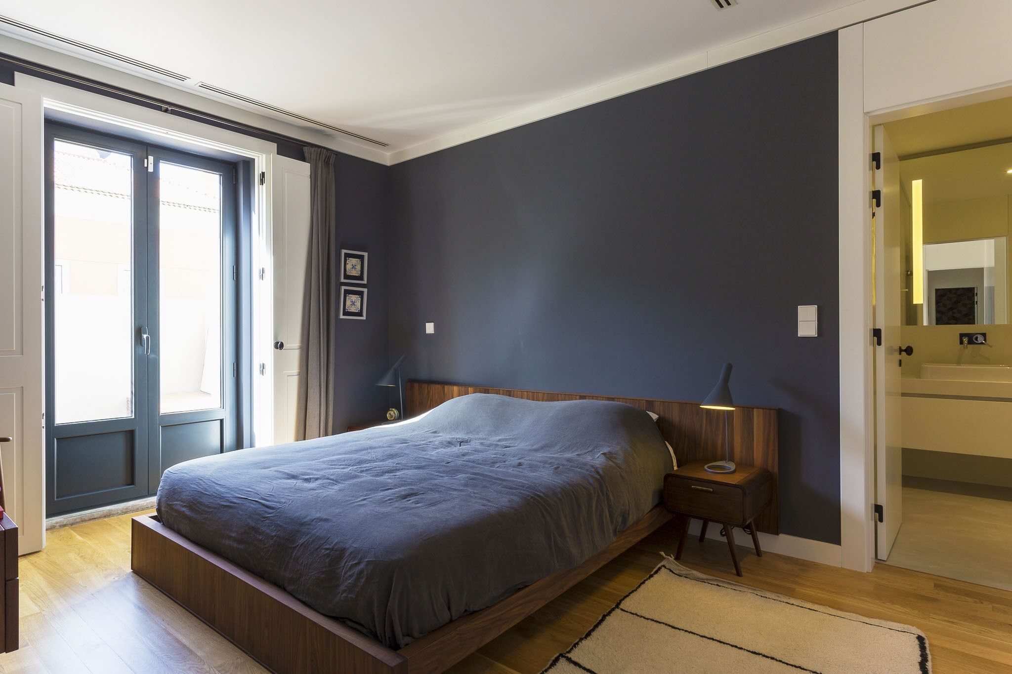 A bedroom with a bed, bedside tables, a nightstand, a door, and a view of the outside.