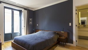 A bedroom with a bed, bedside tables, a nightstand, a door, and a view of the outside.