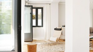 A modern living room with a glass door leading to a balcony, a wooden floor, and a seating area with a chair and a small table.