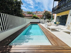 Et rektangulært pool med en træterrasse, omgivet af hvide gelændere og udendørs møbler.