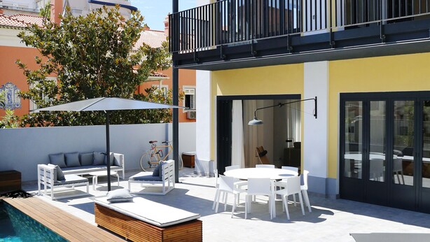 A modern outdoor pool area with a wooden deck, white furniture, and a clear blue pool.