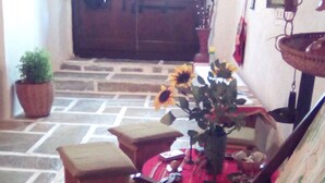 Una stanza con pavimento in pietra, una panca di legno, un tavolo con un cesto d'uva e una pianta in vaso.