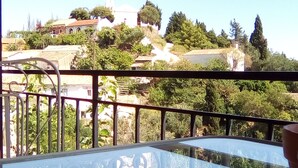 Un balcone con ringhiera in metallo, un tavolo e vista su una città con edifici e alberi.