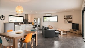 A modern kitchen with a dining area, a grey sofa, and a television in a living room.