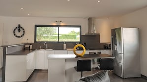A modern kitchen with a central island, stainless steel appliances, and a large window providing a view of greenery.