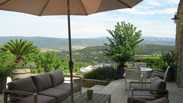 An outdoor seating area with a sofa, chairs, and a table under an umbrella, overlooking a scenic landscape.
