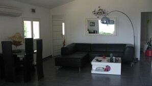A modern living room with a black sofa, a white coffee table, and a dining area with chairs and a table.