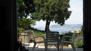 An outdoor patio with a table and chairs, a potted plant, and a view of a coastal landscape.