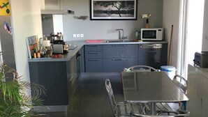 A modern kitchen with a central island, stainless steel appliances, and a dining area with metal chairs.