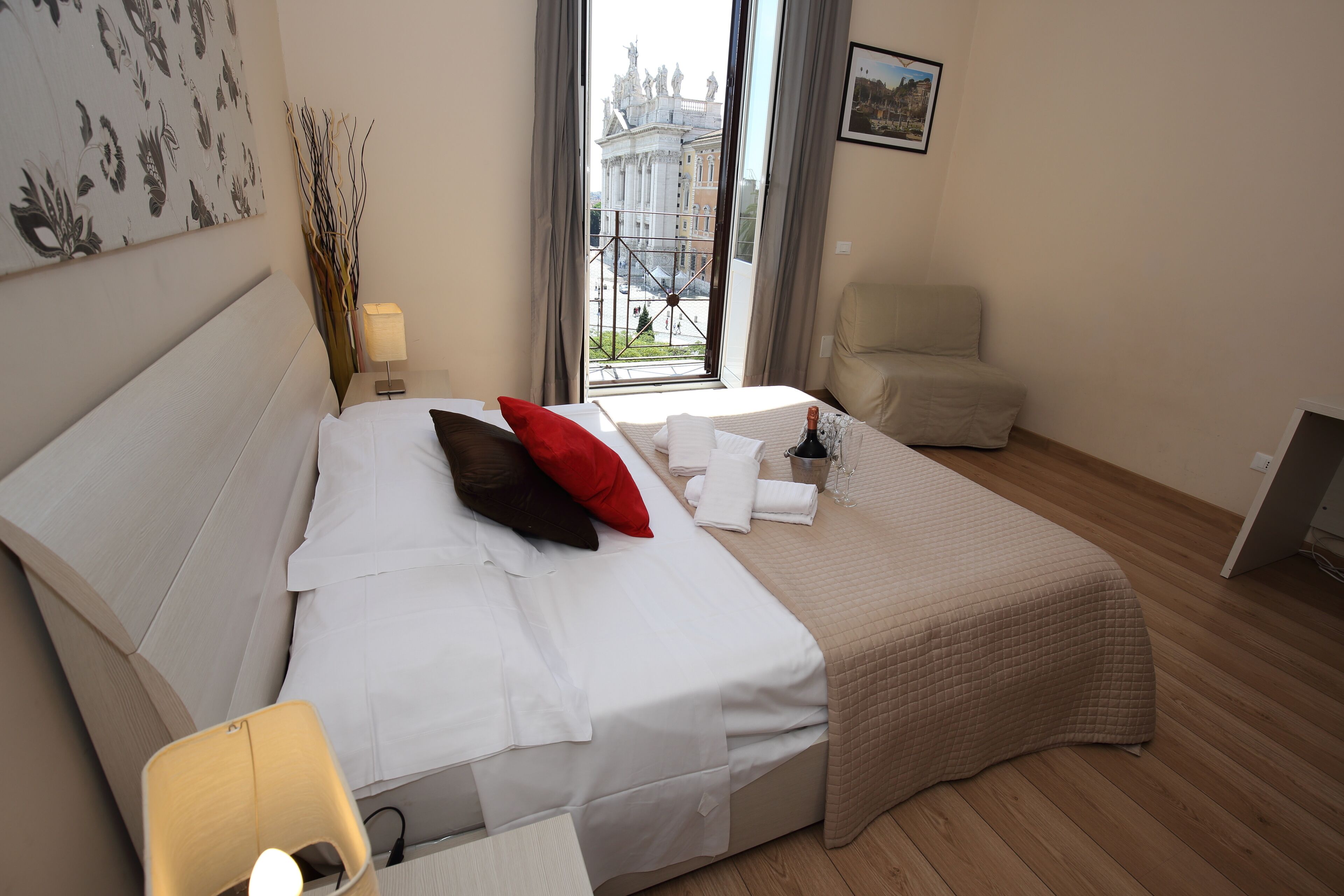 A hotel room with a bed, a chair, a table with a lamp, and a window with a view of a building.