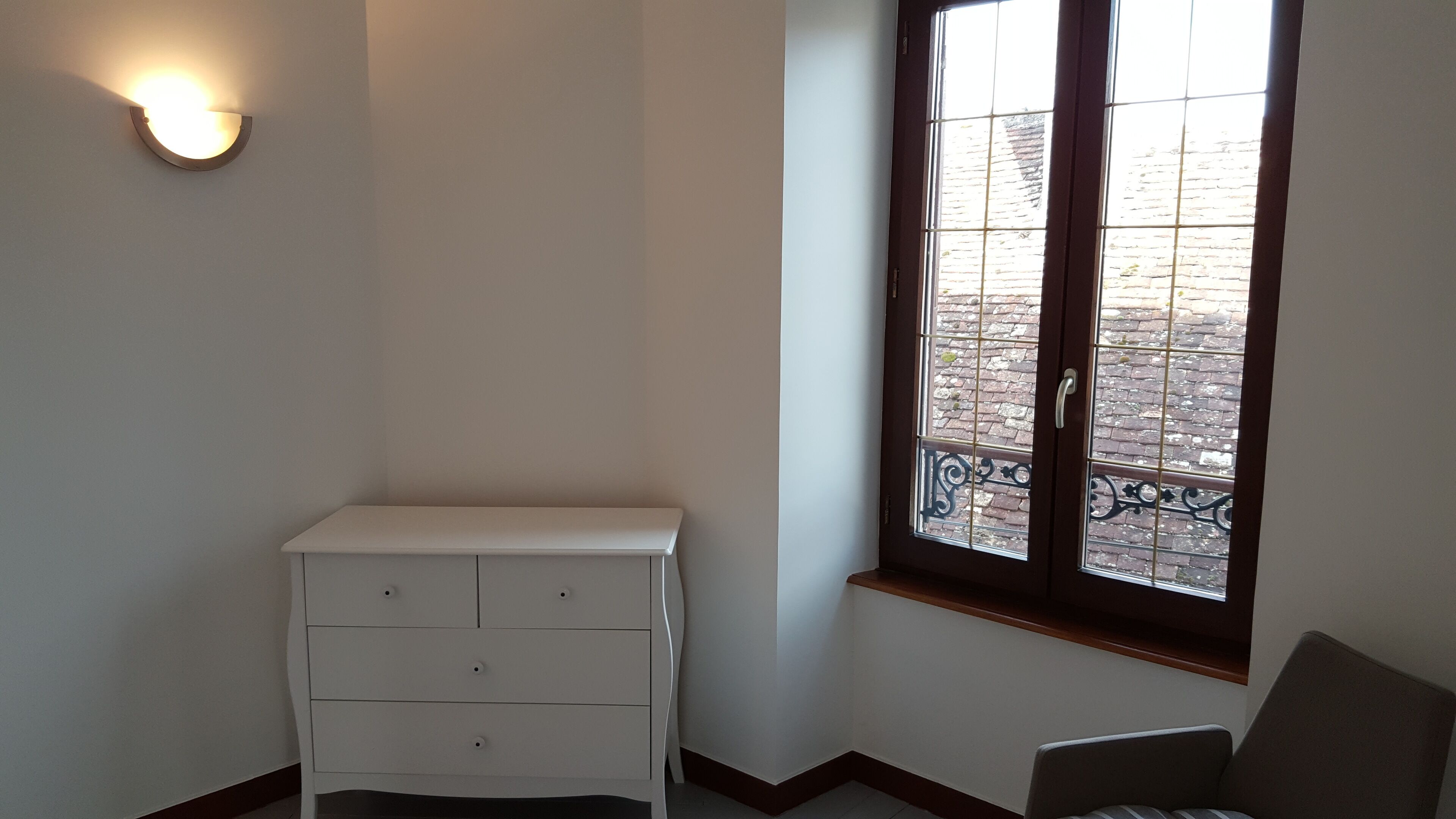 Ein Eckzimmer mit weißem Schminktisch, einem Fenster mit Blick auf ein Backsteingebäude und einer Wandleuchte.