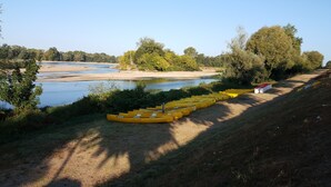 Una fila de kayaks amarillos alineados en un césped junto a un río.