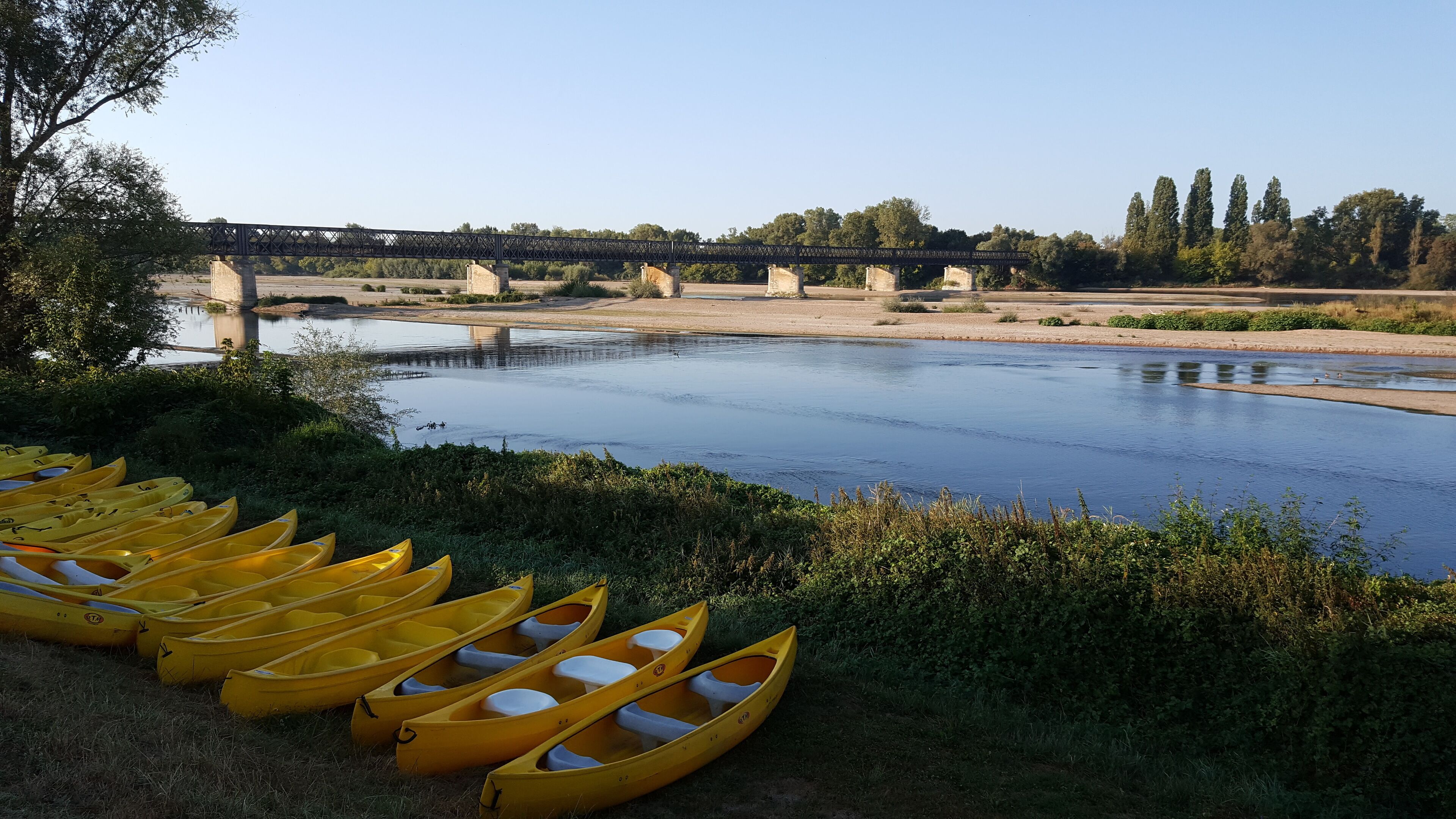 A river with a bridge in the background and yellow canoes lined up on the riverbank.
