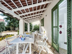An outdoor patio with a table set for dining, surrounded by white chairs, under a wooden pergola. - Villa just a few steps away from the sea of Mazara del Vallo, Sicily (Mazara del Vallo)