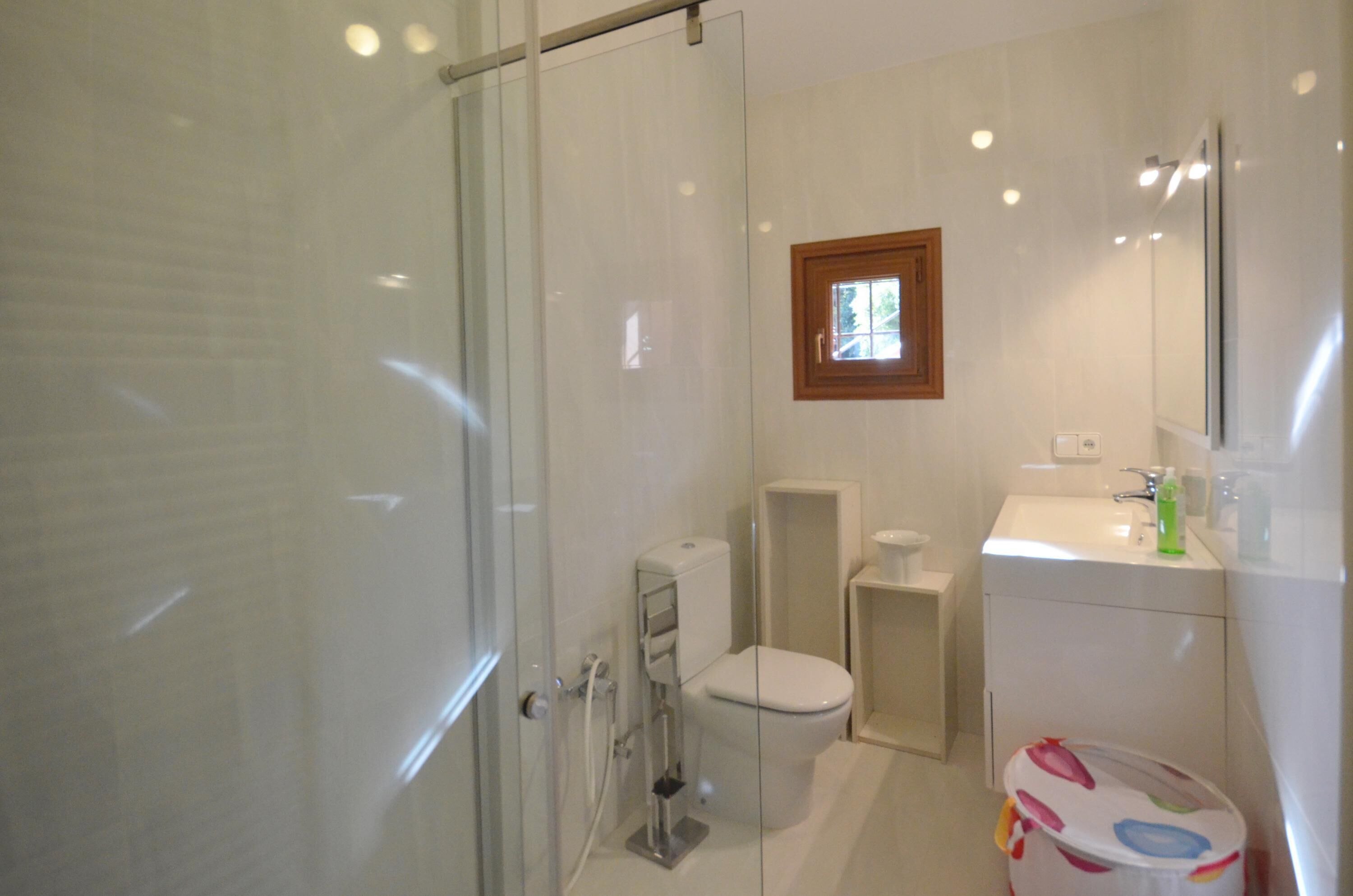 Une salle de bain avec une douche à parois de verre, des toilettes, un lavabo avec un miroir et une petite fenêtre.