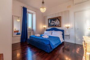 A bedroom with a large bed, a chandelier, a painting, and a window with curtains.