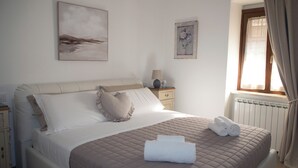 Una cama bien tendida con cubrecama acolchado, una mesita de noche con lámpara y una ventana con cortinas.