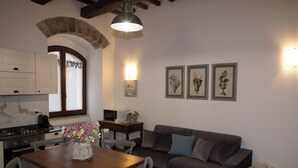 Una cocina con una mesa de madera, un sofá gris y un comedor. Hay cuadros en la pared y un florero con flores sobre la mesa.