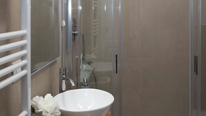 Un baño moderno con ducha envuelta en vidrio, un lavamanos blanco y una encimera de madera.