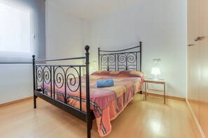A bedroom with a metal bed frame, a wooden bedside table with a lamp, and a window with a view of the outside. - ROYAL MARINE 222 Roses (Rosas / Roses)