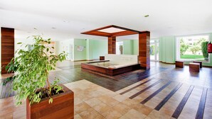 Un amplio vestíbulo de hotel con un gran mostrador de recepción de madera, una zona de estar y una planta en maceta.