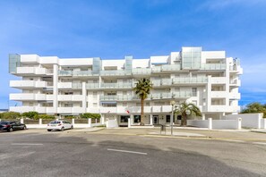 A multi-story white building with balconies, a palm tree in front, and cars parked in front. - ROYAL MARINE 222 Roses (Rosas / Roses)